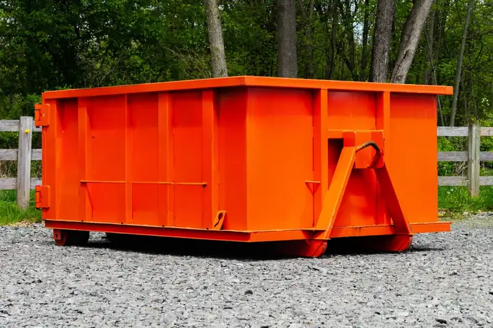 Orange roll-off dumpster parked beside a wood fence